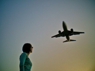 Eine Frau schaut zu einem am Himmel fliegenden Flugzeug auf.