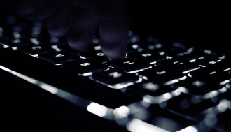 Eine beleuchtete Tastatur im Dunkeln mit einer Hand.